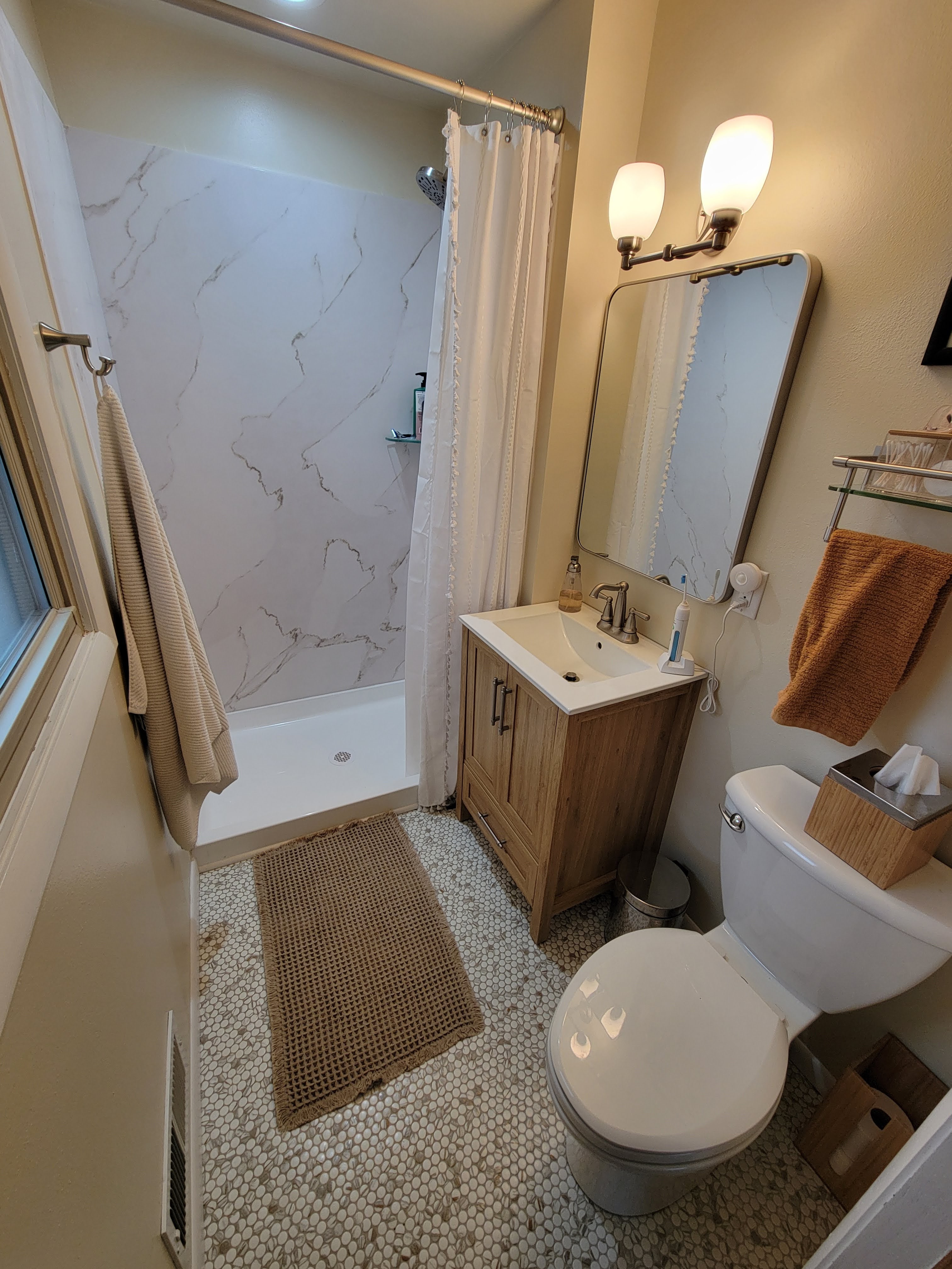 Bathroom after — marble-look walk-in shower, penny tile floor, wood vanity