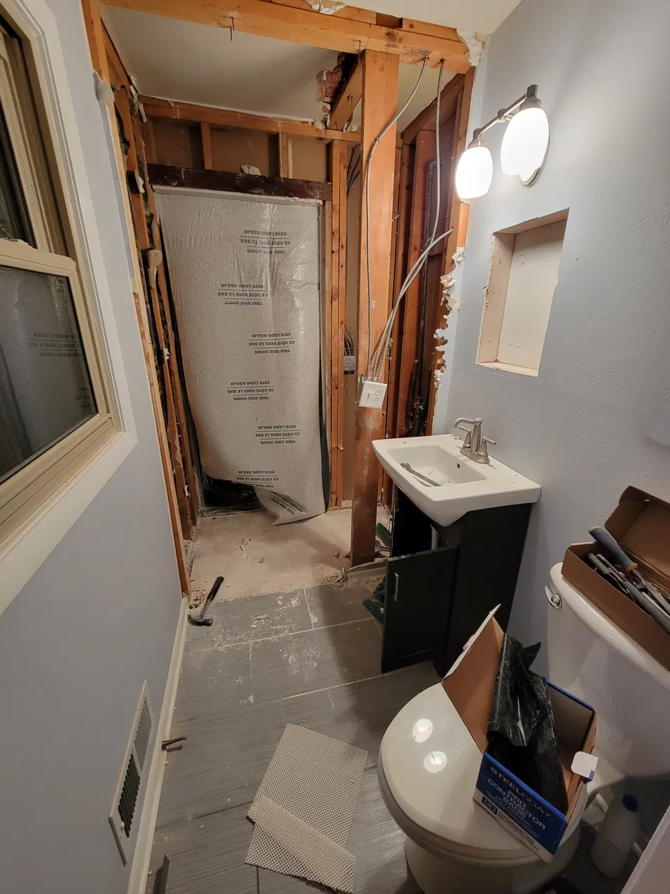 Bathroom before — mid-demo, walls opened up, shower area gutted